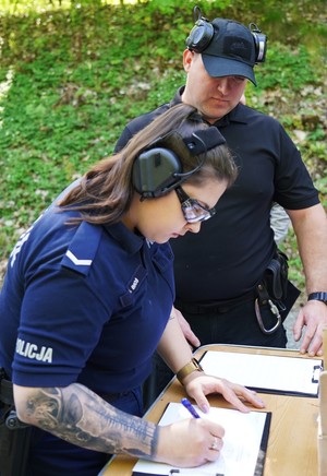 Policjantka podpisuje dokument. Obok niej stoi instruktor.