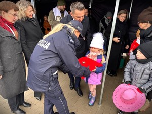 Zdjęcie przedstawia dziecko wręczające policjantce oznakę.